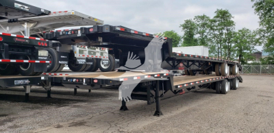 Beavertail trailer on a lowboy with multiple axles and loading ramps, viewed from side angle.