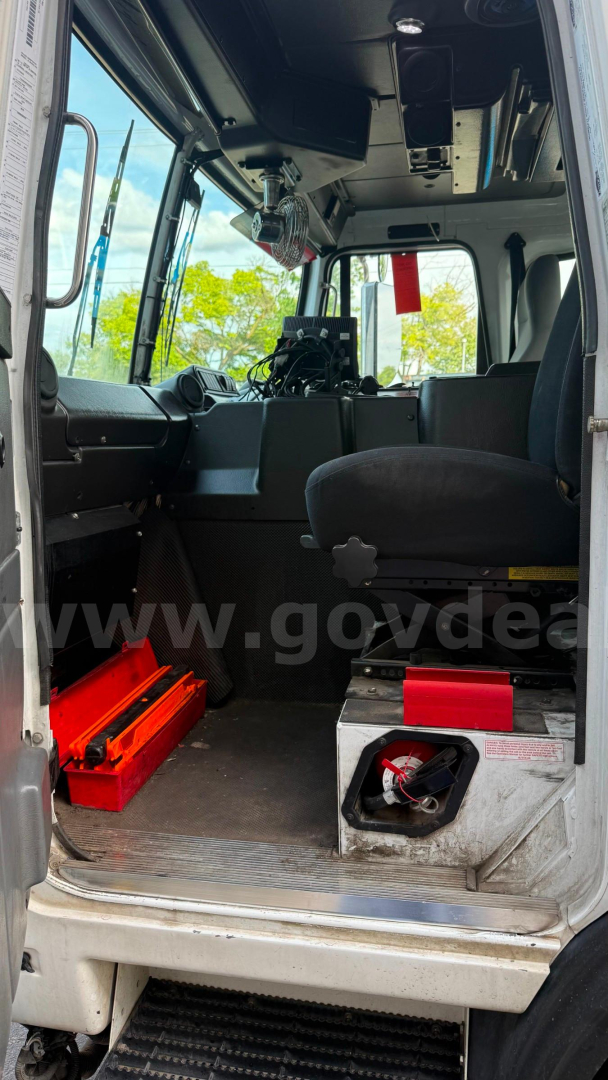 Inside view of 2016 Autocar XPeditor cab showing driver's seat, overhead controls, and tool storage with red toolbox; cockpit with windshield and entry step visible.