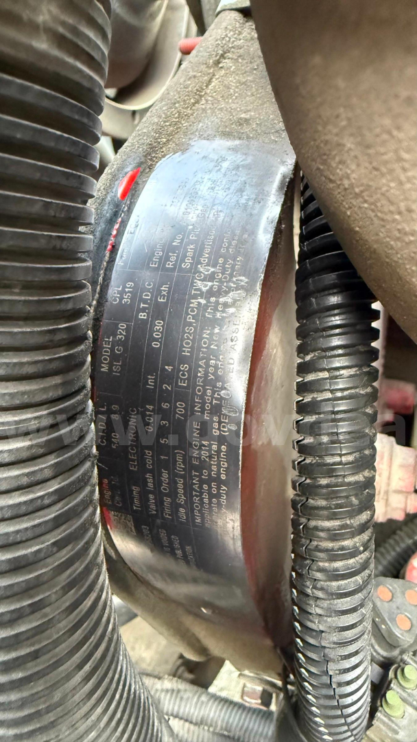 Engine bay label with vehicle specifications and serial numbers visible on a metal plate near hoses and wiring.