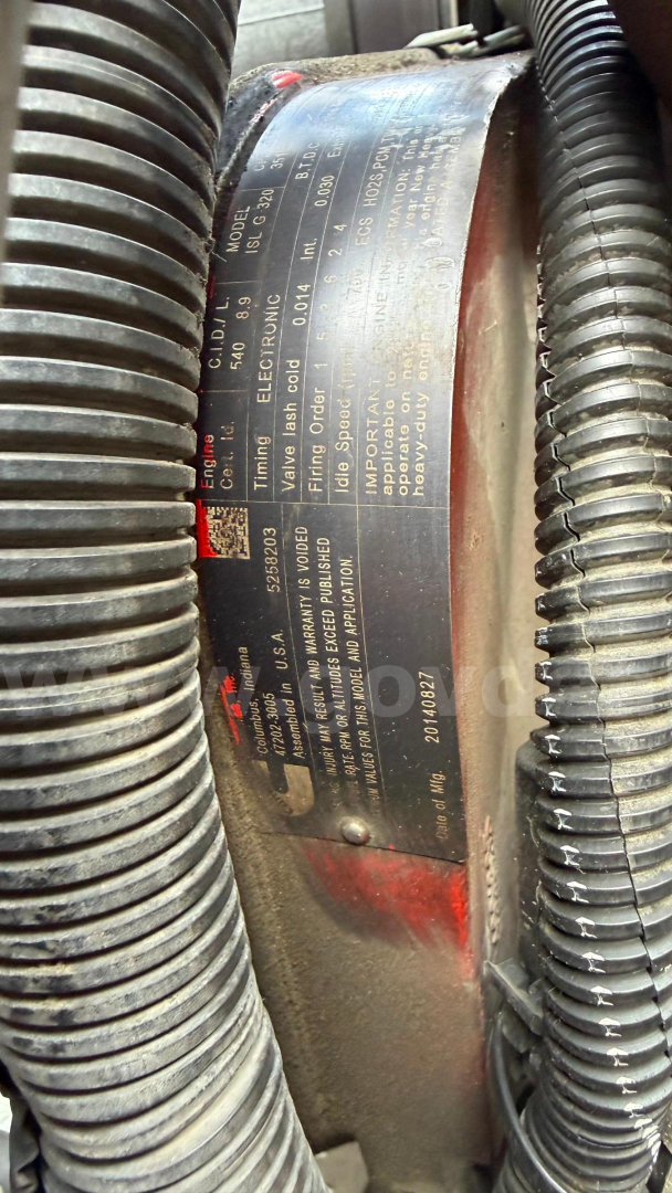 Label plate on engine or component showing specifications and part numbers, framed by flexible hoses.