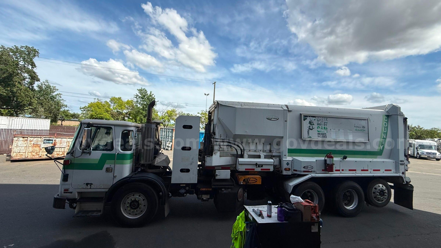 Autocar Xpeditor truck with a green and white cab and a large waste collection body; side view shows a rear cab access door and hydraulic components.