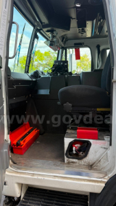 Inside view of 2016 Autocar XPeditor cab showing driver's seat, overhead controls, and tool storage with red toolbox; cockpit with windshield and entry step visible.