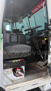 Cockpit of a 2016 Autocar XPeditor truck showing driver seat, steering wheel, dashboard, pedals, and electrical components near floor; warning label and controls visible.