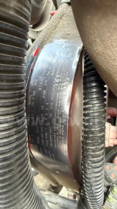 Engine bay label with vehicle specifications and serial numbers visible on a metal plate near hoses and wiring.