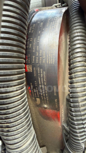 Label plate on engine or component showing specifications and part numbers, framed by flexible hoses.