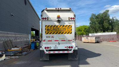 Rear view of 2016 Autocar Xpeditor garbage truck with yellow caution sign, taillights, and rear bumper