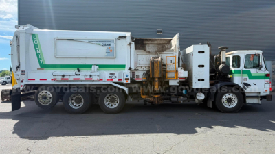 Autocar Xpeditor refuse truck in service with green and white livery, side view showing cargo body and hydraulic compactor mechanism.