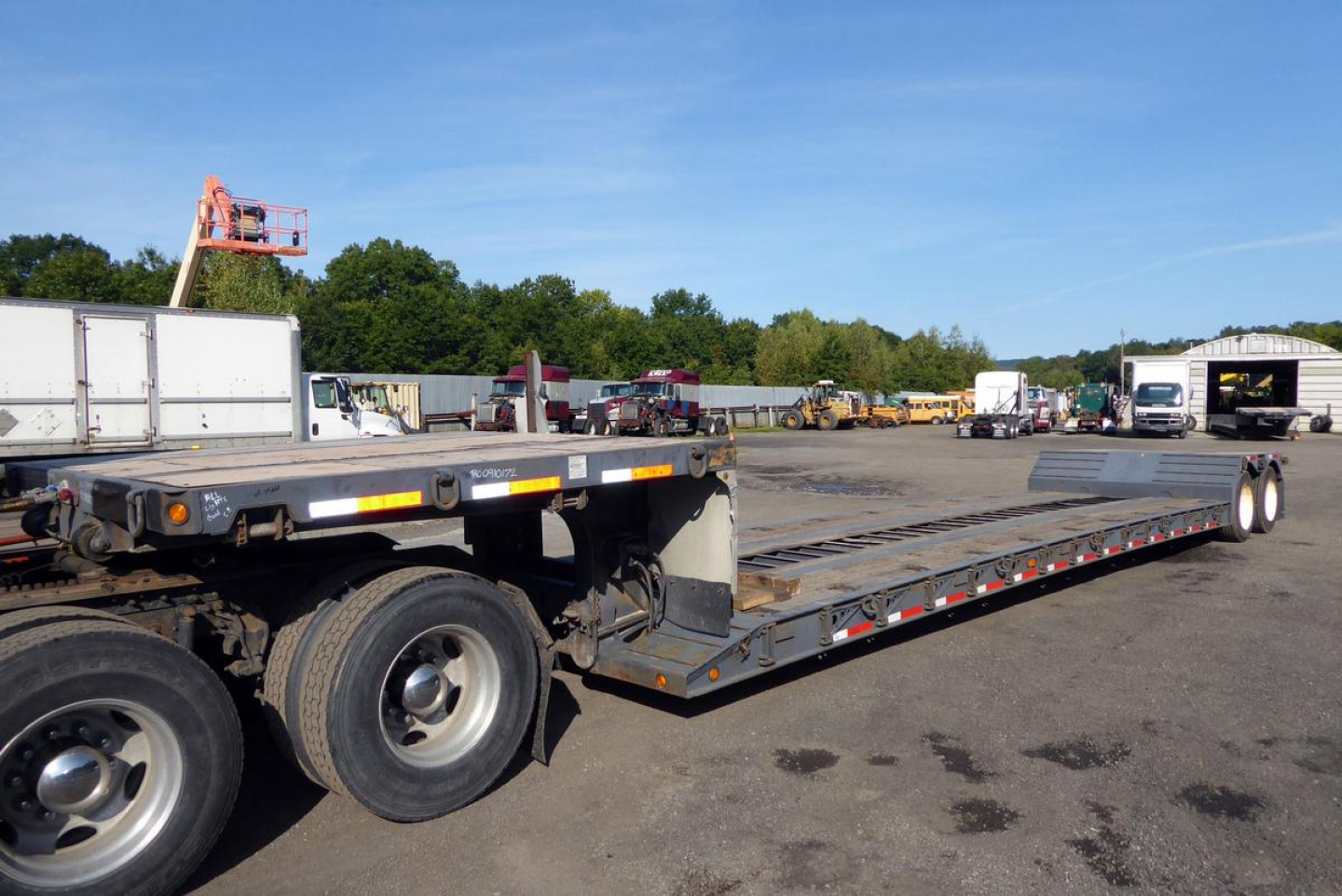 IHI Fontaine trailer showing a long flatbed deck with tandem rear axle and ramps, in a lot with other trucks and trailers.