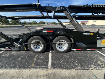 Semi-trailer show side view of a black car carrier trailer with dual axles and metal frame, CX-5308LT branding near midsection.