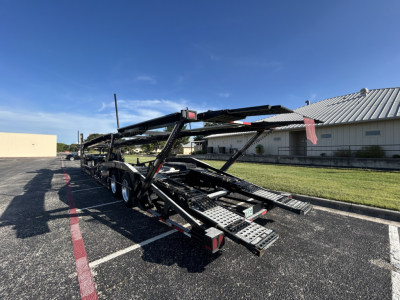 Cottrell CX-5308LT car carrier trailer showing loading ramps and hydraulic arm in service with multiple axles and metal decking.