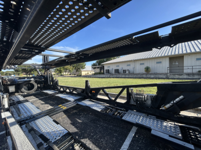 Car carrier trailer interior with metal deck, dual-axle frame, and perforated decking showing structural components and hydraulic equipment.