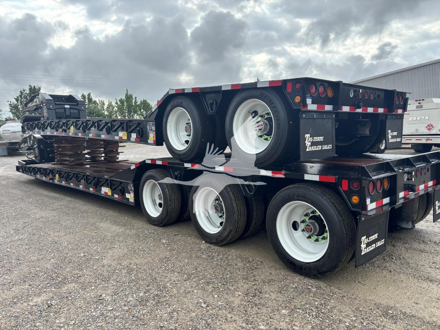 Trailer showing stacked lowboy equipment with multiple axles and white wheels.