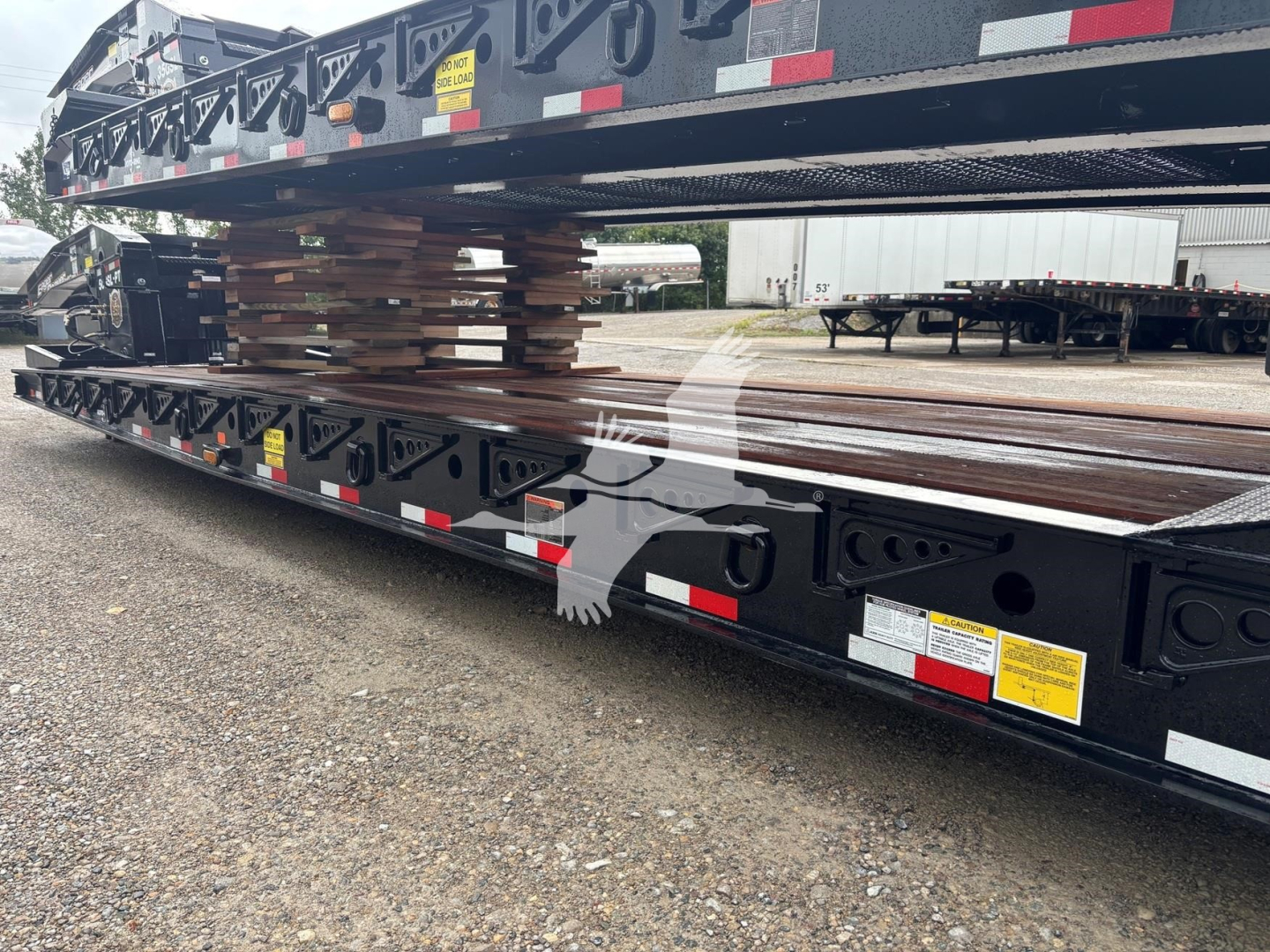 Trailer deck load with steel I-beams and stacked lumber on a lowboy trailer showing labeling and reflective tape.