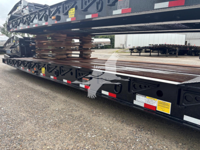 Trailer deck load with steel I-beams and stacked lumber on a lowboy trailer showing labeling and reflective tape.