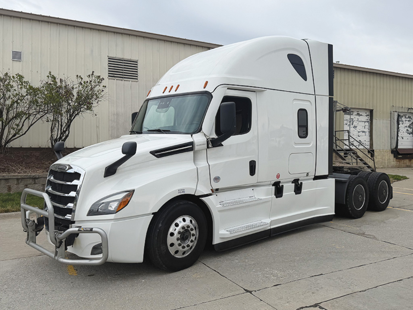 Truck in a parking lot: white 2023 Freightliner Cascadia126 sleeper cab with aerodynamic hood, grille guard, side access steps, and dual rear axles; no visible logos legible besides generic truck features.