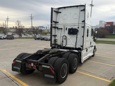 Truck cab rear view of a 2023 Freightliner Cascadia126 sleeper, showing rear chassis, dual rear axles, and mudflaps with Freightliner branding.