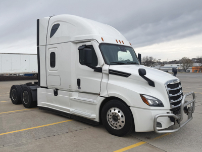 Truck cab showing 2023 Freightliner Cascadia126 with white exterior, sleeper cab, vertical exhaust, and chrome bull bar in a parking lot.