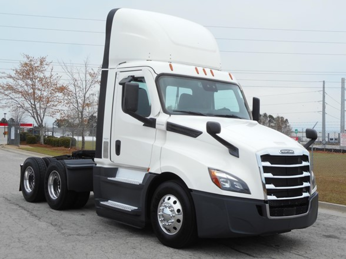 Truck cab showing Freightliner Cascadia 126 day cab with sleeper pod and dual rear axles, white exterior and chrome front grille.