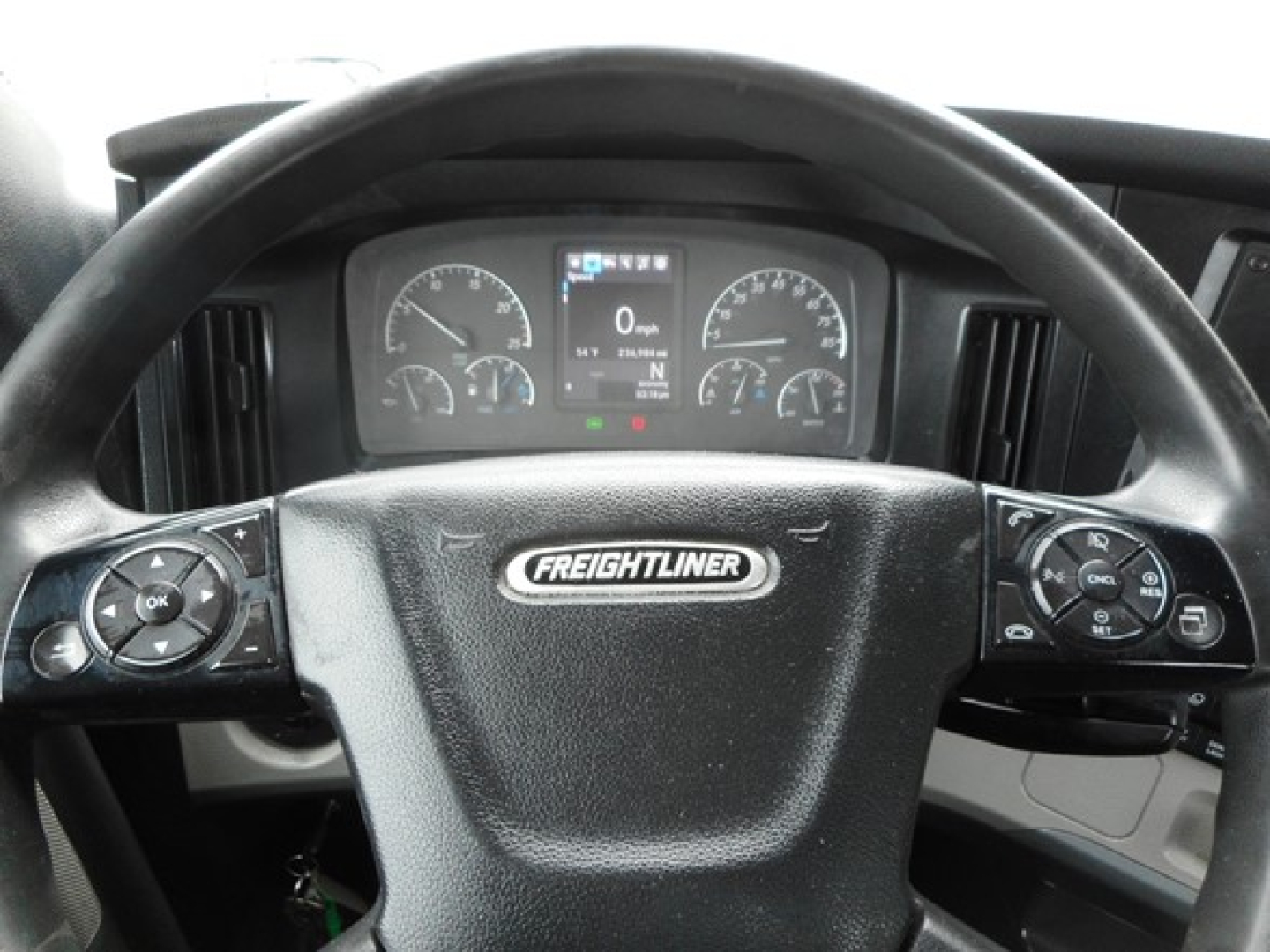 Freightliner Cascadia dash with steering wheel emblem and instrument cluster showing gauges and multifunction buttons on both sides.