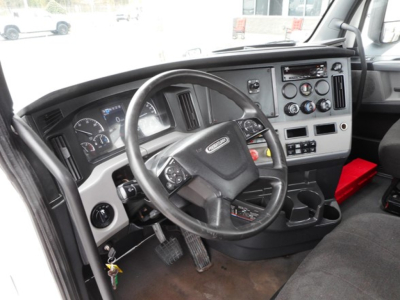 Cabin dash of Freightliner Cascadia 126 showing steering wheel, gauges, and control panel with ignition, pedals visible.