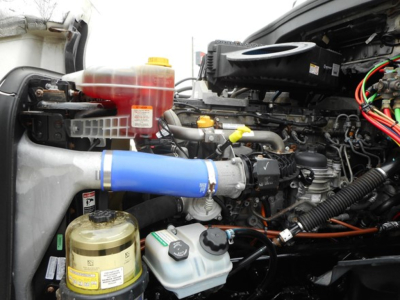 Freightliner Cascadia 126 engine bay showing coolant reservoir, blue intercooler hose, and various fluid reservoirs.