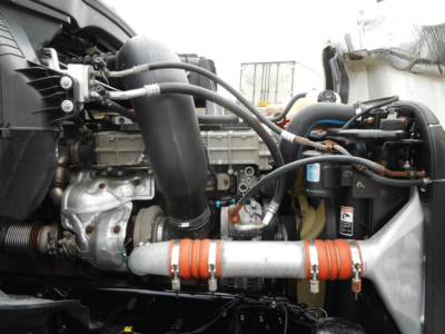 Truck engine bay showing coolant hoses, turbo, intake piping, and orange-wrapped intercooler piping in a Freightliner Cascadia 126 engine compartment.