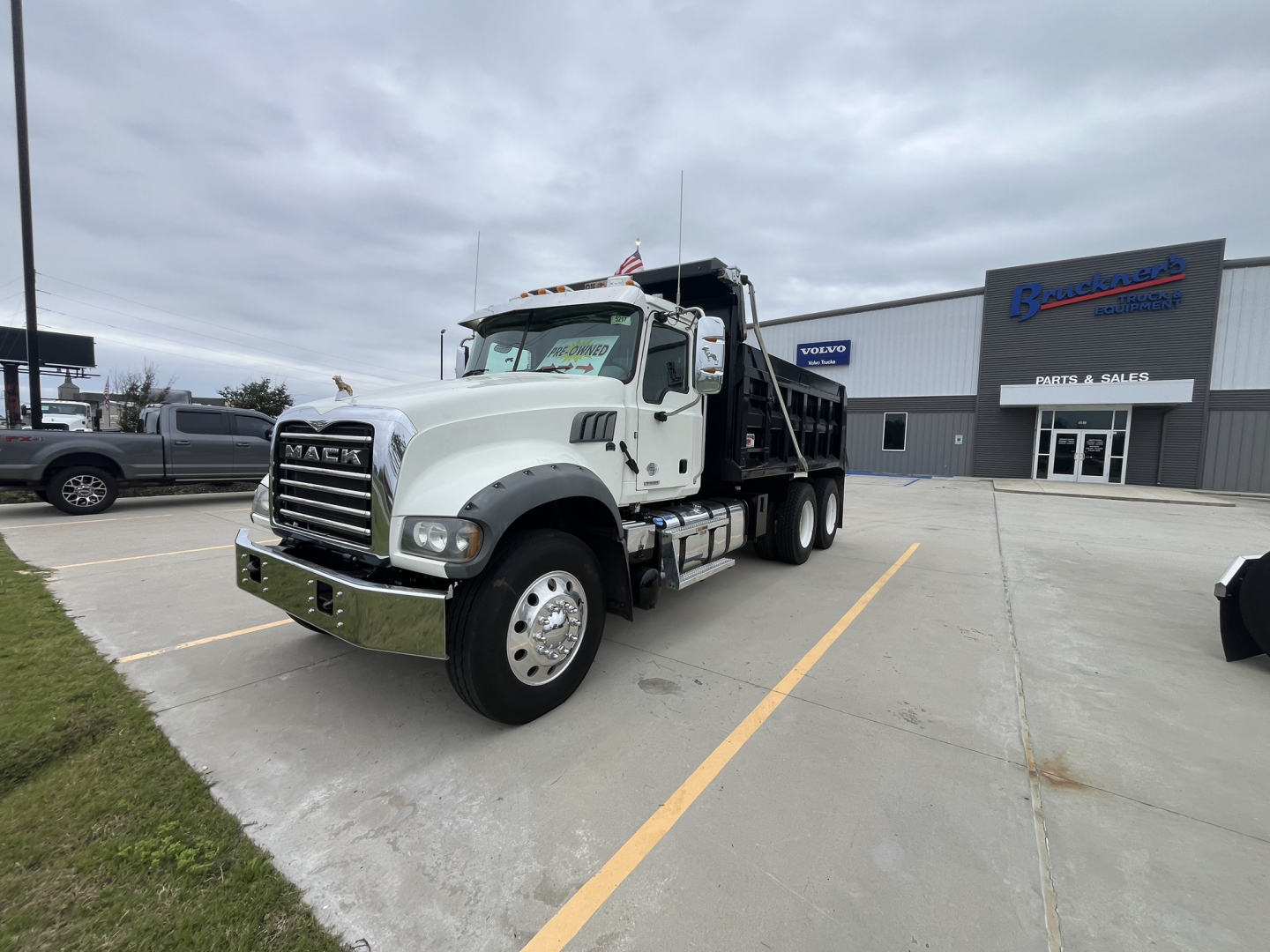 Dump truck 2020 Mack GR64F in-service front-left view showing cab and dump bed, with dealership building in background.