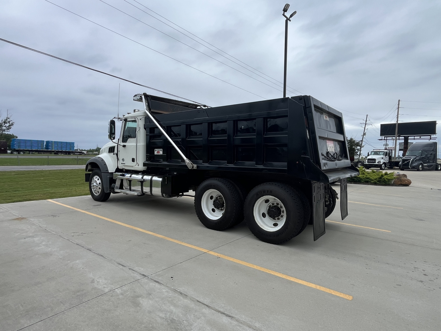 Truck side view showing a black dump bed on a white 2020 Mack GR64F with dual rear axles.