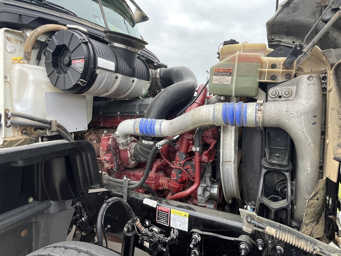 Engine bay of a 2020 Mack GR64F dump truck showing turbo intercooler piping, coolant reservoir, and label stickers visible on components.