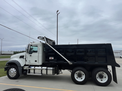 Dump truck side view showing large black dump bed on a white 2020 Mack GR64F chassis with dual rear axles and chrome wheels.