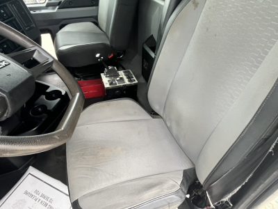 Truck cab interior showing driver seat and passenger seat with center console and exposed metal toolkit; steering wheel on left, cloth seats.