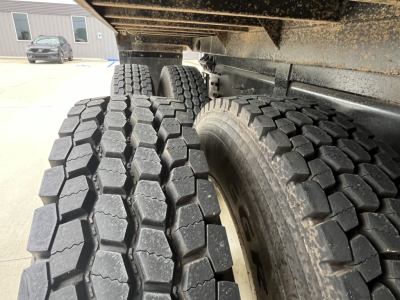 Wheel and dual rear tires of a 2020 Mack GR64F dump truck viewed from underneath near the chassis and undercarriage.