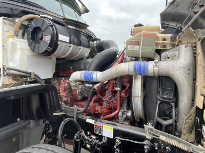 Engine bay of a 2020 Mack GR64F dump truck showing turbo intercooler piping, coolant reservoir, and label stickers visible on components.
