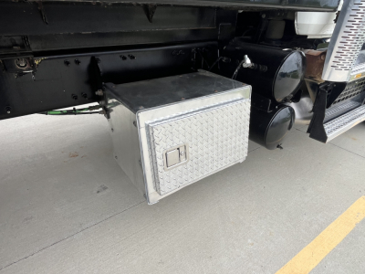 Mack GR64F truck undercarriage showing diamond-plate aluminum storage box mounted under chassis with side-mounted tanks and steps; visible black frame and side panels.