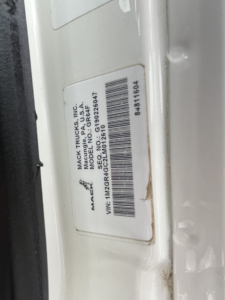Label on Mack truck door jamb showing VIN, stock number, and model details. Text includes 'MACK TRUCKS, INC.', 'MACK TRUCKS', 'GR64F', 'VIN: 1M2GR4GC2LM012610', 'Stock NO: 2604', barcode, and other serials.