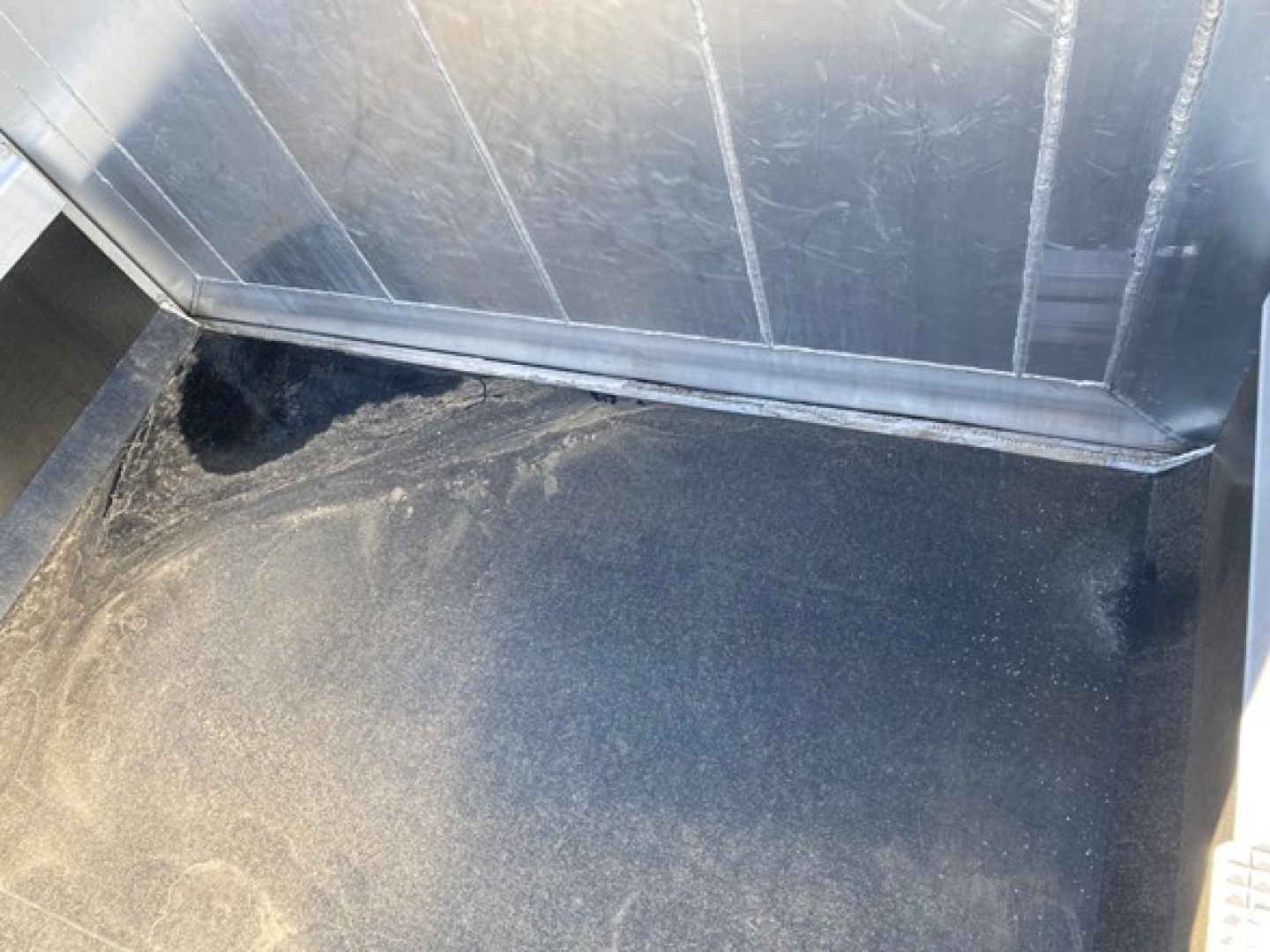 Dump trailer interior showing metal walls and a smooth, dark floor surface.