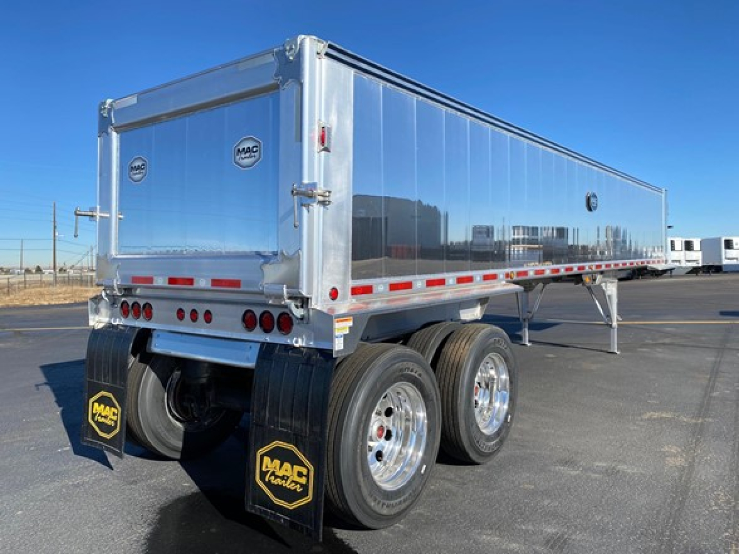 Trailer rear view showing aluminum dump trailer with dual rear axles, MAC Happier logos, LED taillights, and mud flaps in a yard.