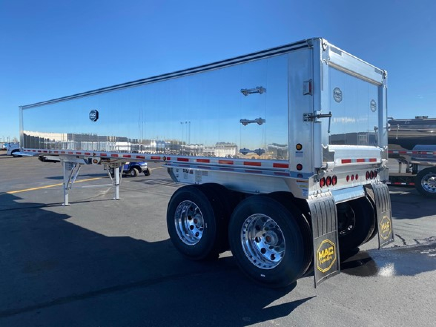 Trailer side and rear view showing a new Mac Western lightweight dump trailer with dual rear wheels, polished aluminum body, rear doors, and mud flaps.