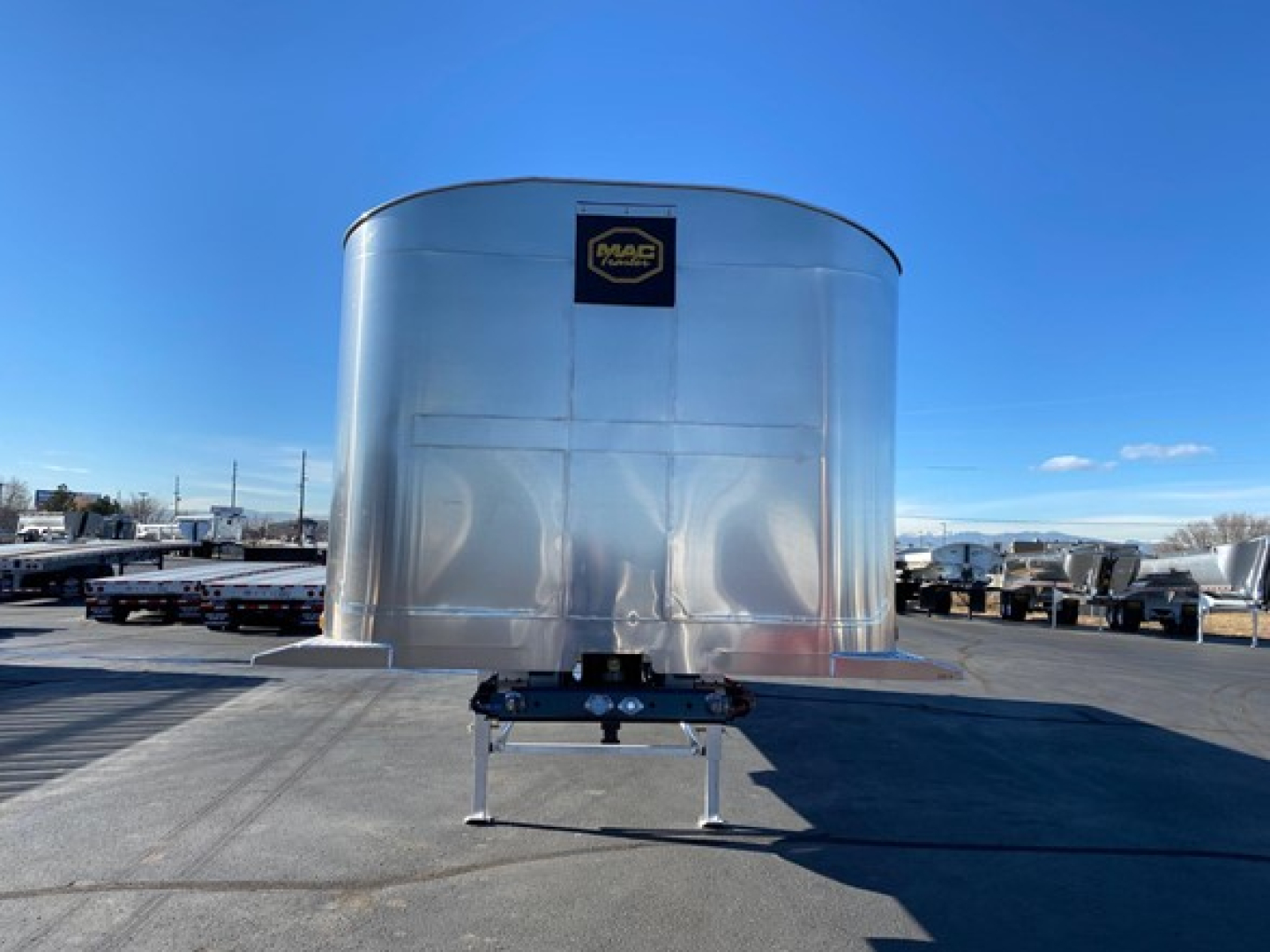 Mac Western lightweight trailer nose view showing shiny silver front, MAC logo, and trailer hitch on a sunny lot.