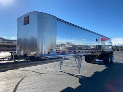 Trailer side view showing new dump trailer with polished aluminum finish and tandem axles under clear sky