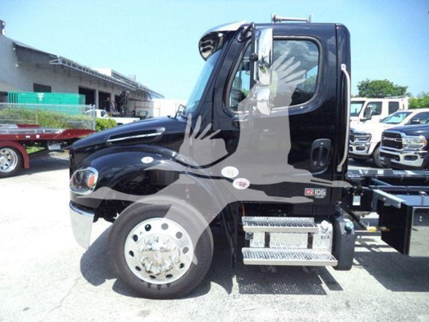 Truck cab side view of a 2027 Freightliner M2 106 Plus rollback unit, black exterior, aluminum steps, dual rear wheels visible, driver's door window, VIN plate not visible.