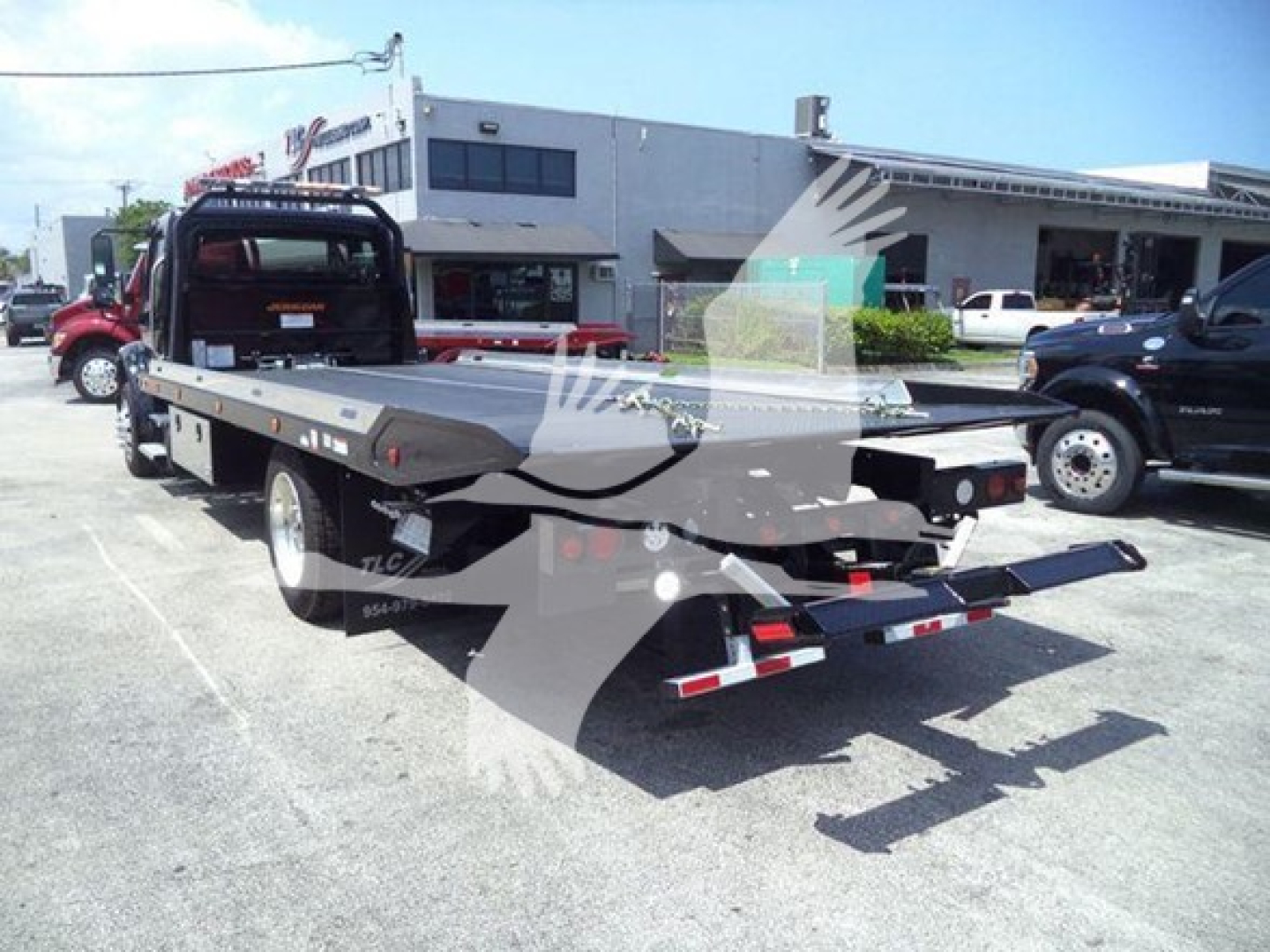 Freightliner M2 106 Plus rollback truck with flatbed and tow setup, viewed from rear-left in parking lot.