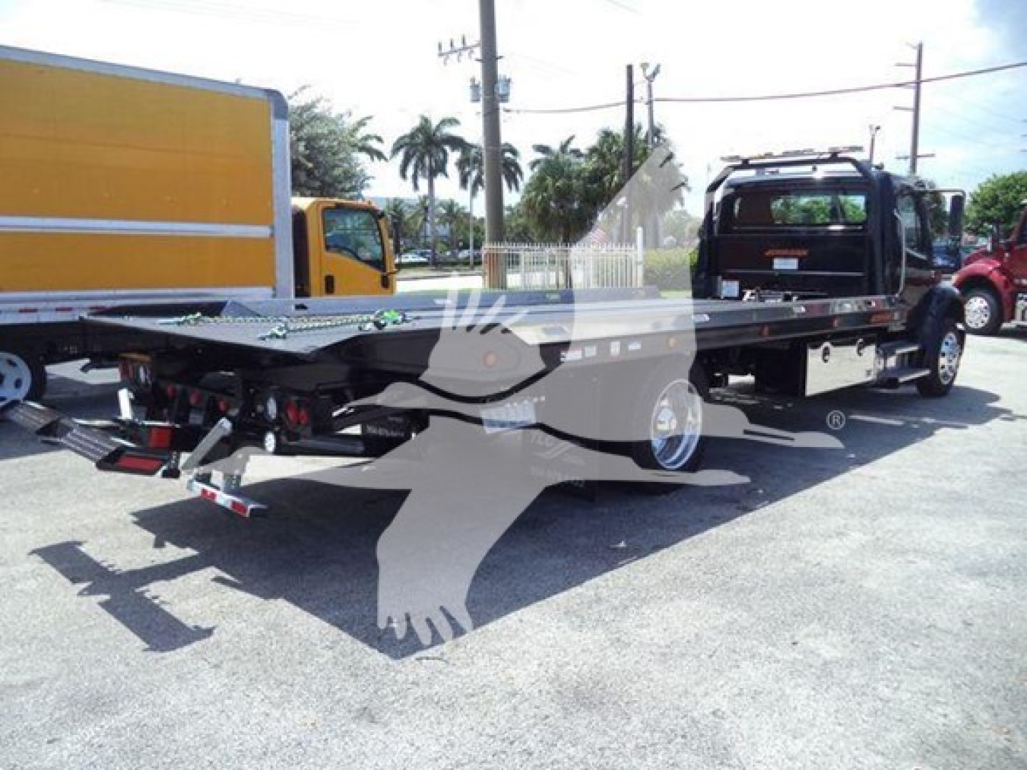 Freightliner M2 106 Plus rollback truck chassis with flatbed and wheel lift in view; license plate not visible; some text on decals or stickers not legible.
