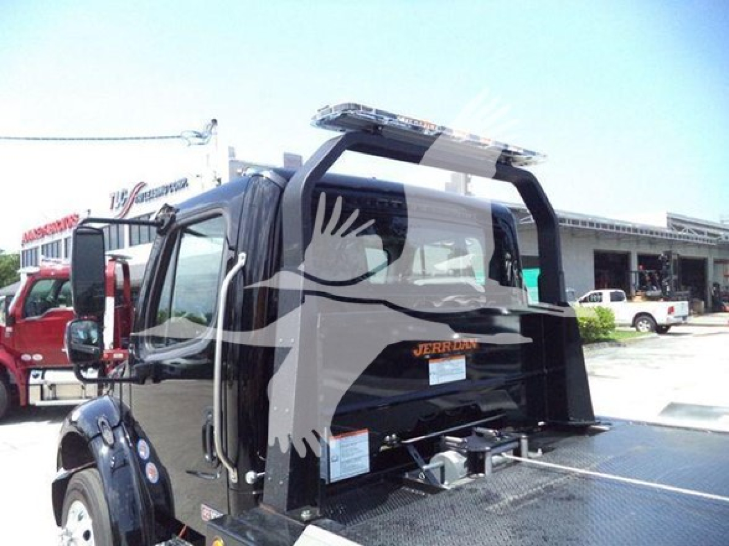Freightliner M2 106 Plus rollback truck rear view showing hydraulic tow setup and rear cab window, black paint.