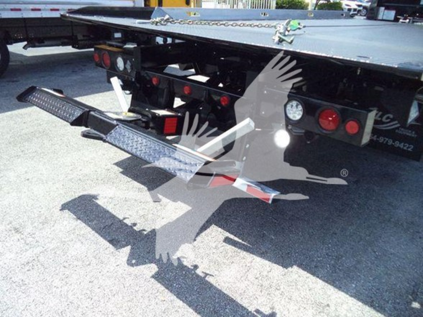 Truck trailer with a loading ramp and rear bumper of a Freightliner M2 106 Plus showing metal steps and taillights.