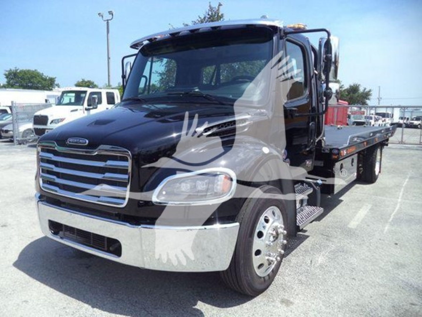Freightliner M2 106 Plus rollback truck in black with chrome grille and flatbed. Visible text includes Freightliner emblem on grille, side mirrors, and a large watermark of a bird logo across the image.