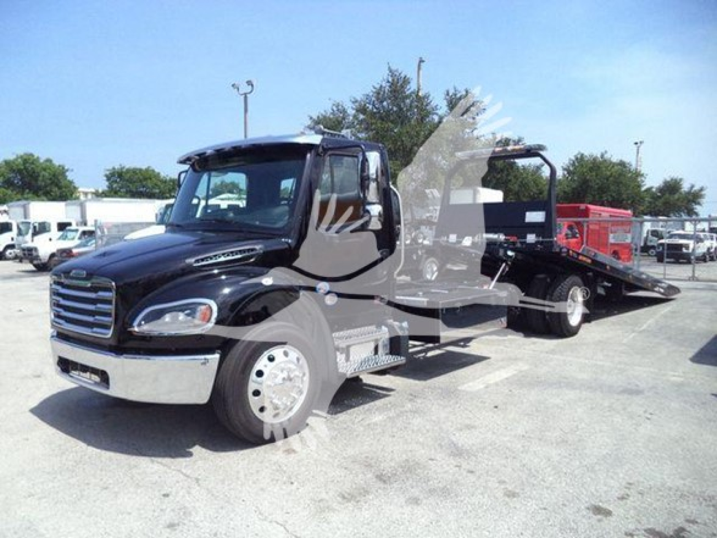 Freightliner M2 106 Plus roll-back truck in a parking lot with a flatbed/rollback bed. Visible text on truck includes no legible labels from distance.