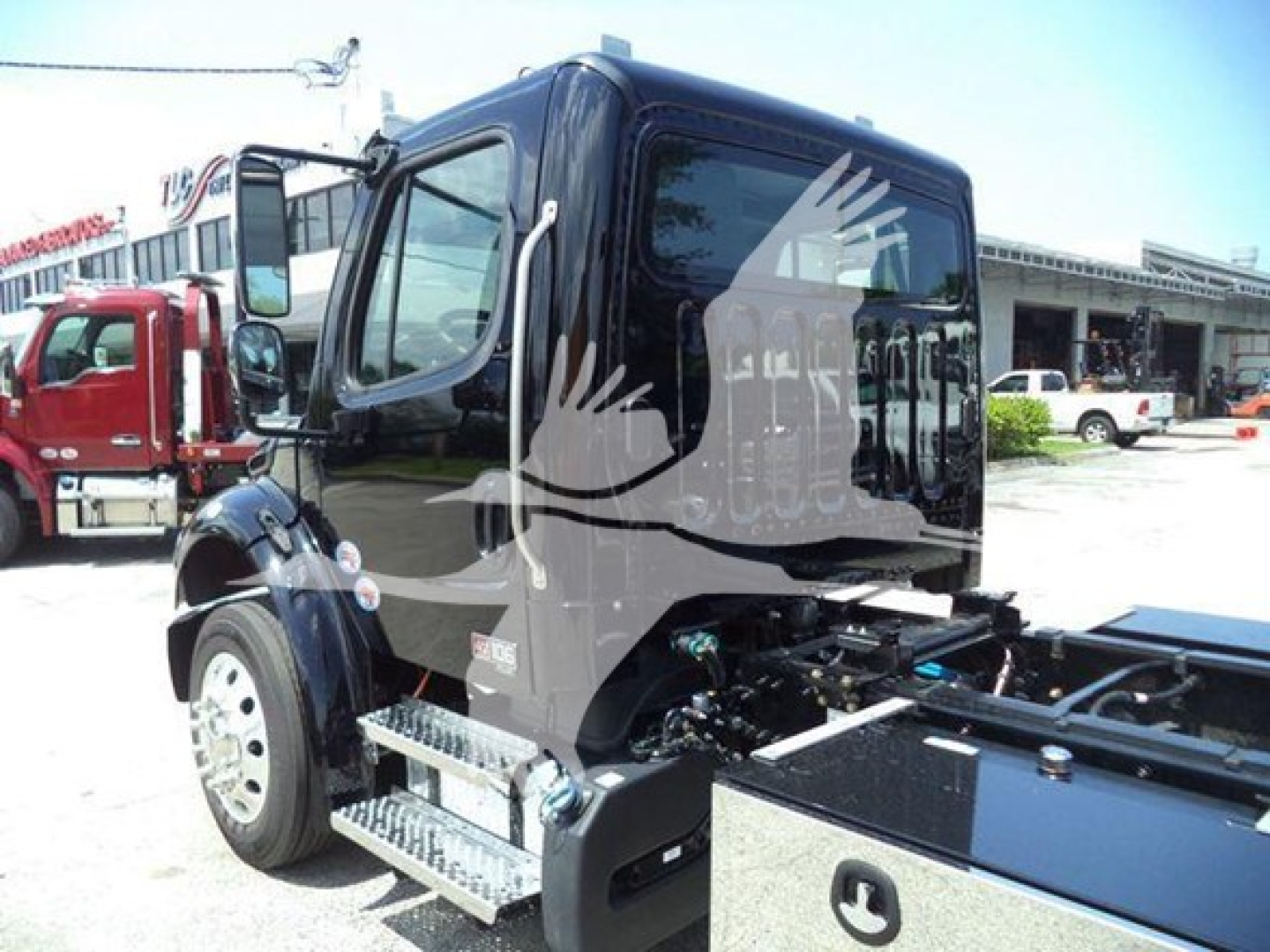 Freightliner M2 106 Plus truck cab and chassis in a dealership lot with side steps and black cab.