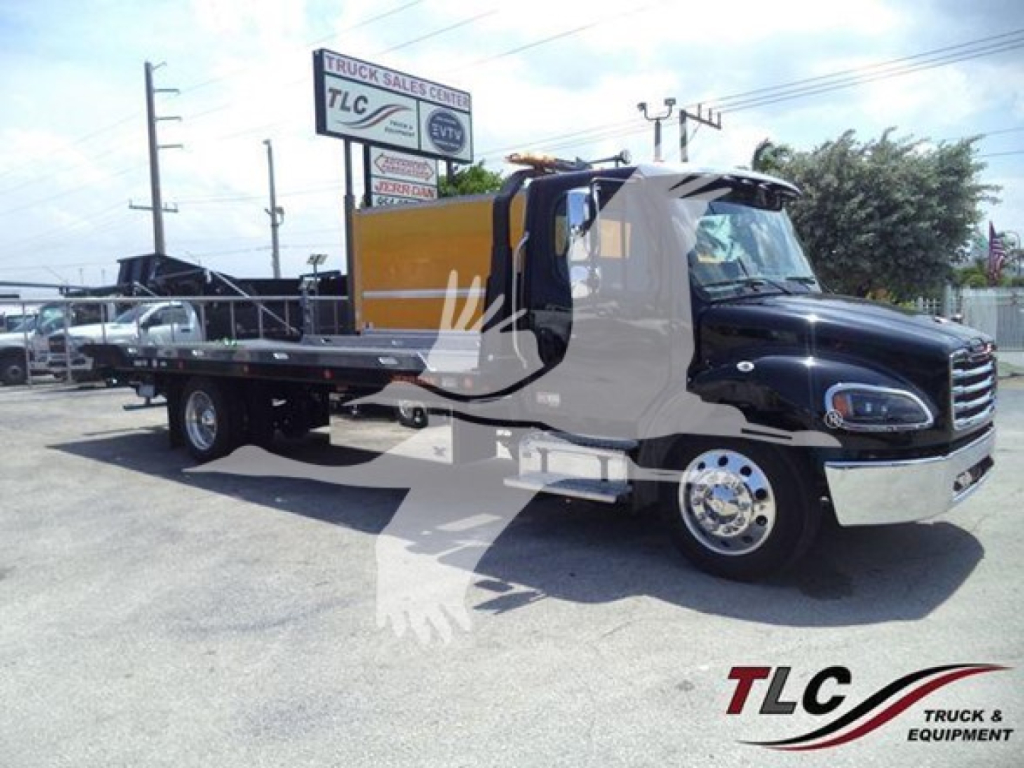 Freightliner M2 106 Plus rollback truck in a dealership lot, black cab, yellow storage unit, chrome wheels, side view shows long flatbed with winch. visible text includes TLC Truck Sales Center sign in background.