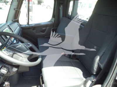 Freightliner M2 106 Plus truck interior driver seat and dashboard visible; steering wheel and control panel on left; cab seating area with large windows.
